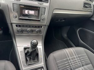 Innenraum eines Autos mit manuellem Getriebe, graue Sitze, Bildschirm zeigt Parksensoren.