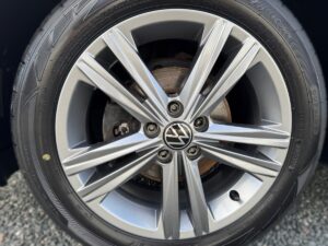 Nahaufnahme eines silbernen Autoreifens mit VW-Logo und detaillierten Felgenspeichen.