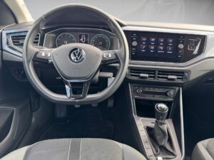 Innenraum eines Autos mit schwarzem Lenkrad und Display; VW-Logo sichtbar.
