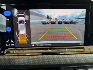 Autodisplay zeigt Rückfahrkamera-Ansicht mit mehreren Autos und farbigem Korridor, sonniges Wetter.