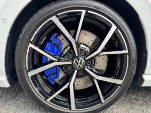 VW-Autoreifen mit schwarzer Felge und blauem Bremssattel, vor einem grauen Hintergrund.