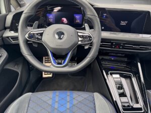 Das Lenkrad und Armaturenbrett eines modernen Autos mit blauer Ziernaht und digitalen Anzeigen.
