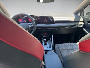 Innenraum eines Autos mit schwarzen und roten Sitzen, modernem Armaturenbrett und Digitalanzeige.