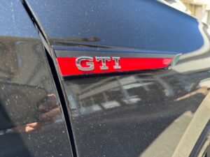 Nahaufnahme eines schwarzen Autos mit "GTI"-Abzeichen und Reflexionen auf dem Lack.