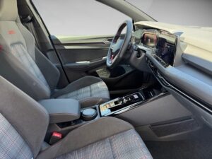Innenraum eines modernen Autos mit grauen Sitzen, rot karierten Details und einem digitalen Display.