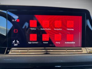 Bildschirm eines Autos mit rotem Interface und App-Symbolen, wie Telefon und Navigation.