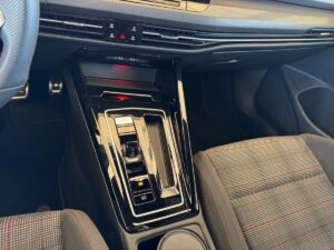 Nahaufnahme der Mittelkonsole eines Autos mit glänzend schwarzem Finish und karierten Sitzen.