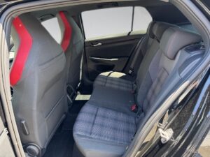 Rücksitze eines schwarzen Autos mit roten Akzenten und kariertem Stoff, interessanter Innenraum.