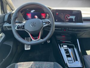 Lenkrad eines Volkswagen Golf GTI, digitales Display, rot-schwarze Details, moderne Bedienelemente.
