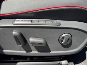 Sitzverstellungen und Kontrollen an einem Autositz in schwarzem Leder mit roten Nähten.