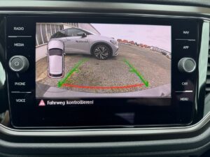 Rückfahrkamera-Bild: Auto vor Gebäude mit Warnanzeige unten. Fahrzeug in Grautönen.