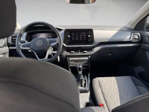 Innenraum eines Autos mit grauen Sitzen; Lenkrad mit Logo; Touchscreen auf Armaturenbrett.
