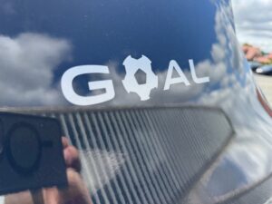 Rückansicht eines schwarzen Autos mit dem Wort "GOAL" in Weiß, das einen Fußball als O zeigt.