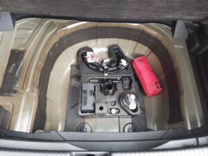 Kofferraum mit Reserveradmulde, Autoteilen und roter Erste-Hilfe-Tasche, grau und ordentlich.