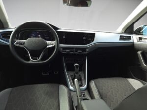 Innenraum eines Autos mit schwarzem Lenkrad und modernen Armaturen, graue Sitze, informatives Display.
