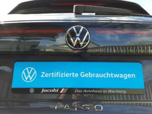Rückansicht eines Volkswagen mit einem Schild "Zertifizierte Gebrauchtwagen" auf blauer Platte.