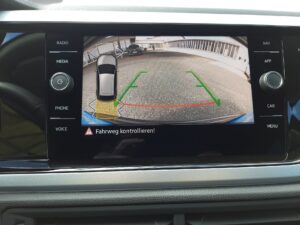Bildschirm zeigt Rückfahrkamera mit Parkplatzansicht, grüne Linien und Warnung.