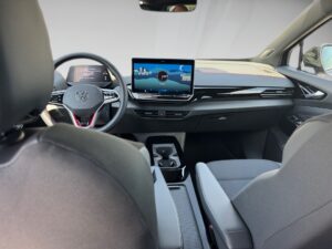 Innenansicht eines Fahrzeugs mit digitalem Display und dunkelgrauen Sitzen.