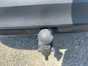 Nahaufnahme einer Autoanhängerkupplung mit abgenutzter schwarzer Kugel auf Kiesuntergrund.