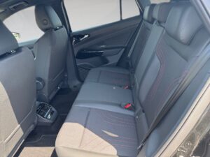 Rücksitz eines Autos mit grauen Polstern und roten Nähten, sonnig beleuchtet.