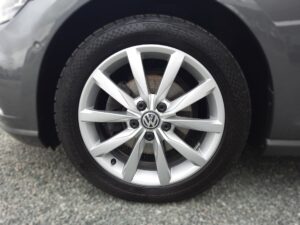 Nahaufnahme eines silbernen VW-Rads mit klar sichtbarem Firmenlogo auf einer Kiesfläche.