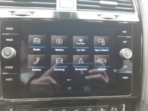 Beleuchteter Auto-Touchscreen mit Apps wie Radio, Medien, Navigation, zwei Hände spiegeln sich.