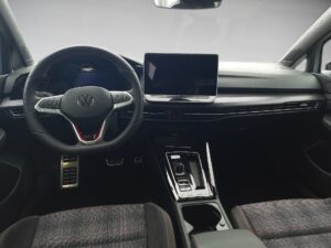 Innenansicht eines VW-Fahrzeugs, schwarzes Armaturenbrett, Touchscreen, hellgraue Sitze.