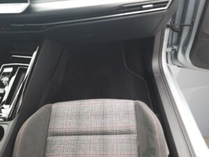 Autositz im Inneren eines Autos mit grauem Stoff und roten Streifen; modern gestaltet.