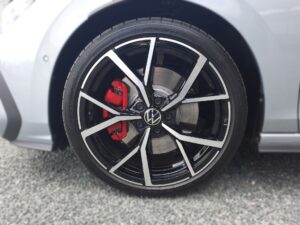 Nahaufnahme eines Autoreifens mit silbernen Felgen und roten Bremssätteln auf grauem Untergrund.