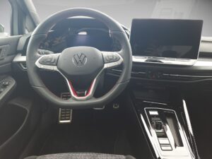 Innenraum eines Autos mit einem Volkswagen-Lenkrad und Bildschirm, schwarzes modernes Design.