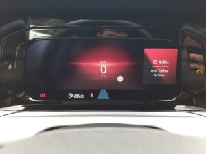 Digitales Tacho eines Autos, zeigt 0 km/h. Bildschirm ist schwarz mit roten Akzenten.
