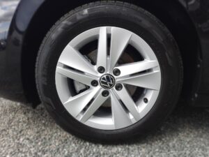 Silberne Autoreifenfelge mit VW-Logo auf Kieselboden.