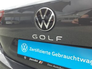 Heckansicht eines grauen VW Golf mit reflektierendem Firmenlogo und blauem Zertifizierungsschild.