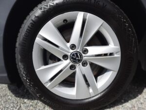 Auto-Reifen mit silberner Felge und VW-Logo auf Asphalt. Profiliertes Reifenmuster.