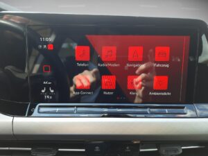 Nahaufnahme eines Fahrzeuginfotainmentsystems mit rotem Hintergrund und Apps. Spiegelndes Display.