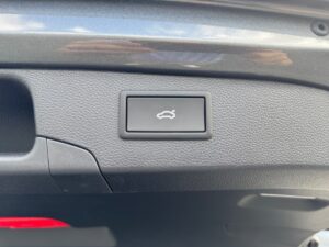 Kofferraumknopf in einem Auto, grau und schwarz, mit Icon eines geöffneten Kofferraums darauf.