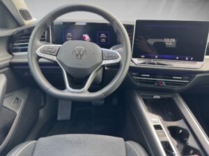 Innenansicht eines VW mit schwarzem Lenkrad, großen Displays und grauen Sitzen.