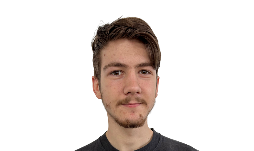 Ein junger Mann mit Bart schaut neutral, trägt ein dunkelgraues T-Shirt.