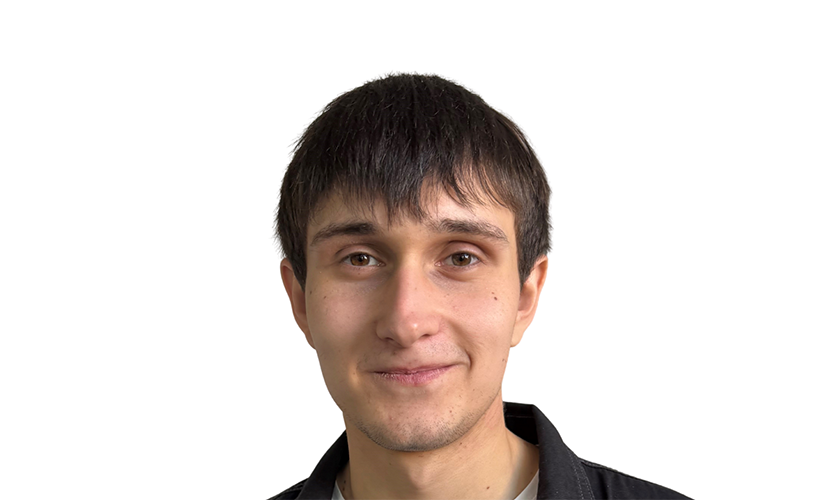 Eine lächelnde Person mit dunklem Haar und einem schwarzen Hemd vor weißem Hintergrund