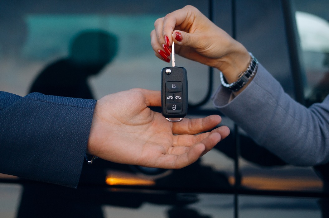 Frau gibt Autoschlüssel an Mann. Hände halten Autoschlüssel. Autovermietung